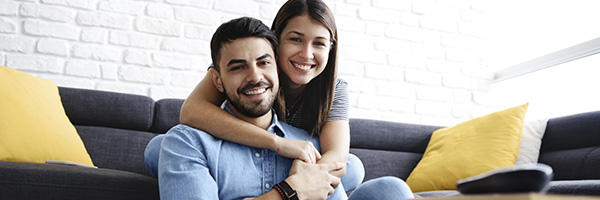 Seguro de Accidentes RGAProtección Accidentes - Pareja joven sonriendo en el salón de su casa con portátil